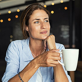 Frau hält Kaffee-Tasse in der Hand und schaut aus dem Fenster