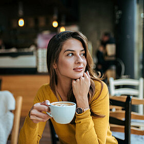 Frau sitzt in einem Kaffe und blickt gedankenversunken in die Ferne